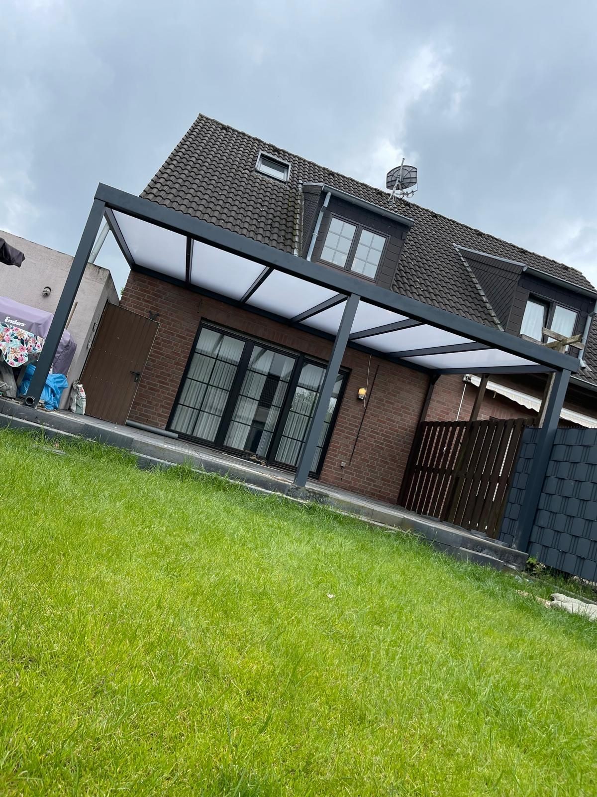 Modern house with a patio cover and a large green lawn under a cloudy sky.