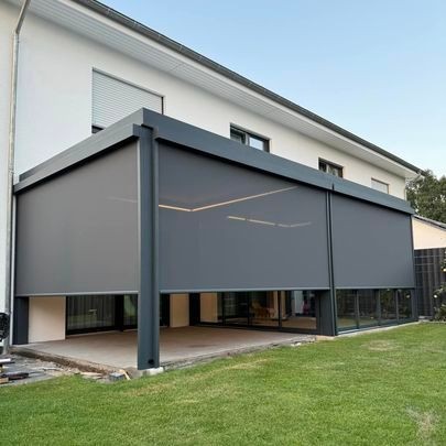 Modern house with a covered patio and gray retractable sun shades next to a green lawn.