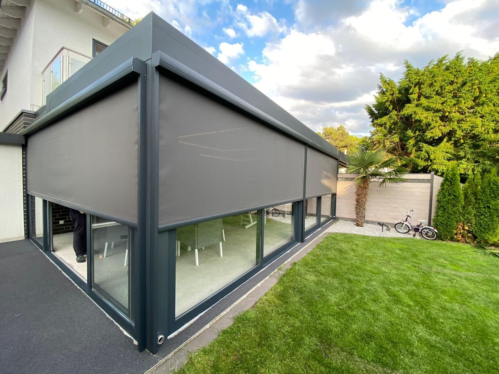 Modern patio enclosure with gray screen shades, adjacent to a grassy yard and a palm tree.