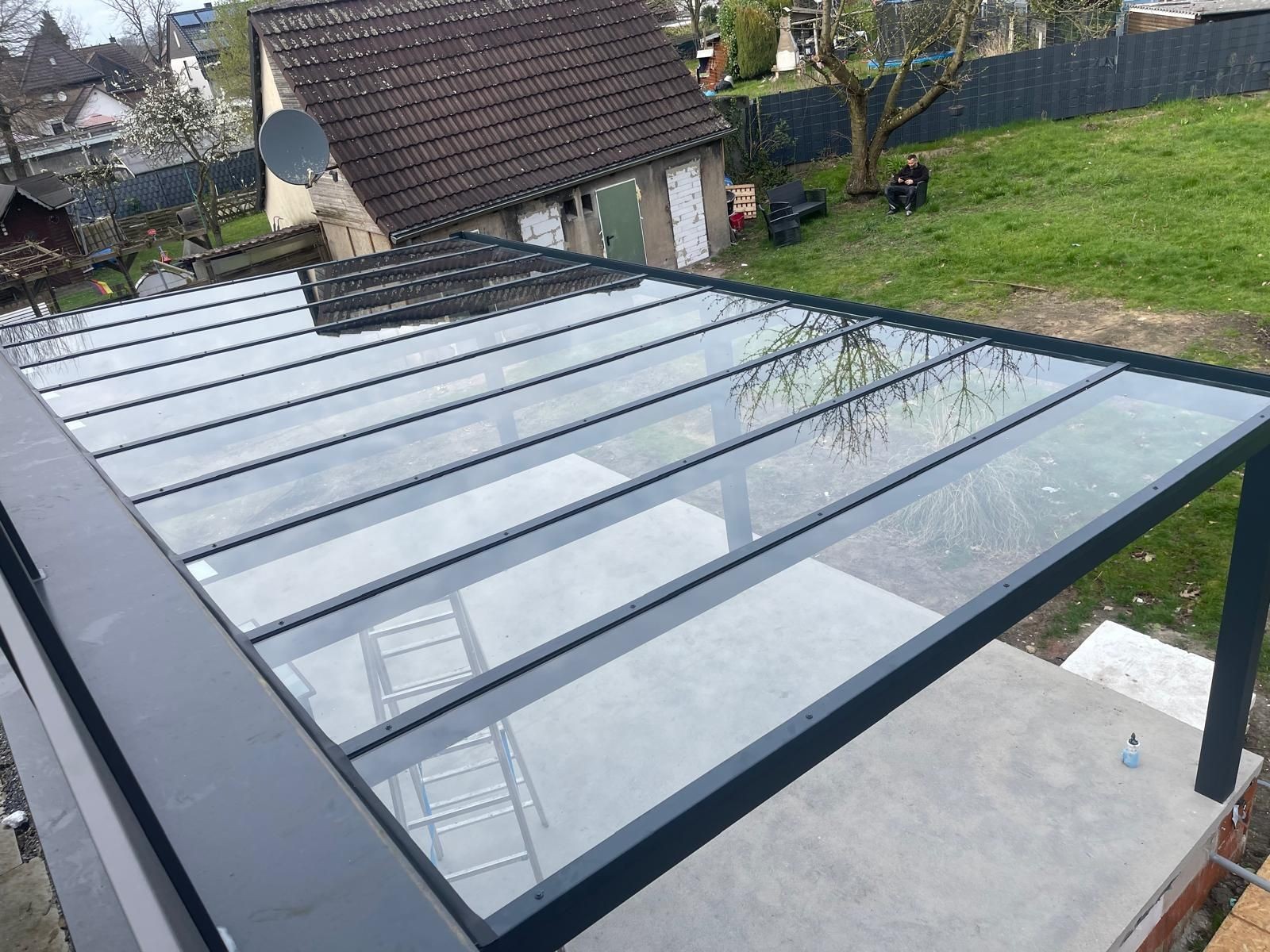 Glass patio roof with metal frame overlooking a backyard with grass and outdoor seating.